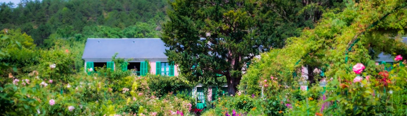 a dirt lane leads to a small house which is nearly obscured by the garden and trees in front of it
