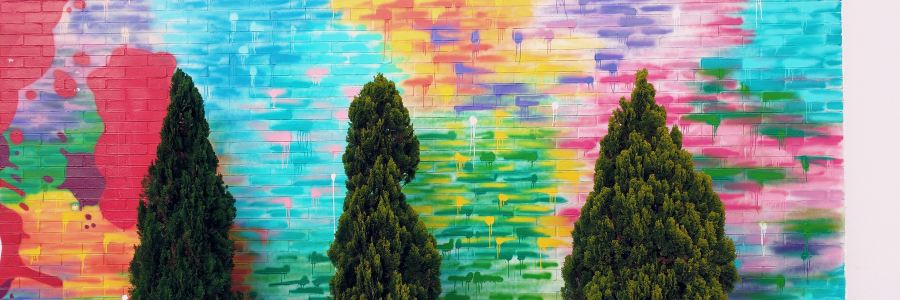 topiary spaced apart from each other backed by a colorful mural on a brick wall